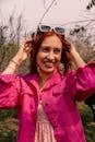pexels-photo-27619514-27619514 Smiling woman in a vibrant pink jacket enjoying a sunny day outdoors with stylish accessories.